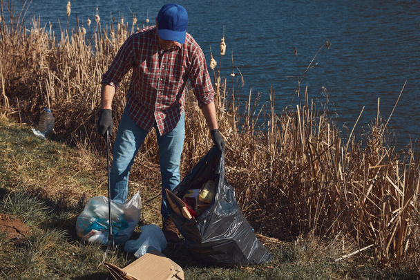 Dobrovolník a aktivista v oblasti životního prostředí čistí špinavý břeh jezera plný odpadků. - Fotografie, Obrázek