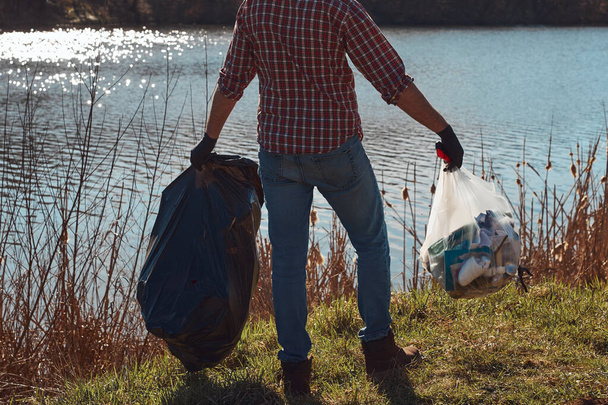 Wolontariuszka i aktywistka ekologiczna sprzątająca brudne brzegi jeziora wypełnione śmieciami. - Zdjęcie, obraz