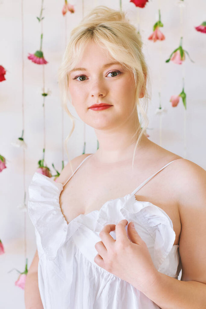 Studio portrait of pretty young teenage 15 - 16 year old girl wearing summer dress, posing on white background with hanging flowers, beauty and fashion concept - Foto, Imagen