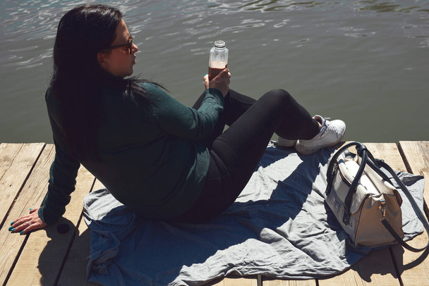 Женщина в белых кроссовках отдыхает в солнечный день на деревянной палубе озера. - Фото, изображение
