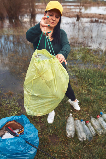Wolontariuszka i aktywistka ekologiczna sprzątająca brudne brzegi jeziora wypełnione śmieciami. - Zdjęcie, obraz