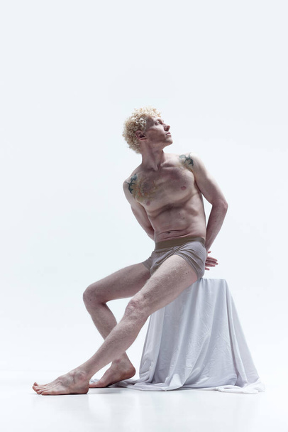Portrait of attractive mature man with blond curly hair in underwear, posing shirtless over white studio background. Like antique sculpture. Concept of male body aesthetics, mens beauty, art, ad - 写真・画像