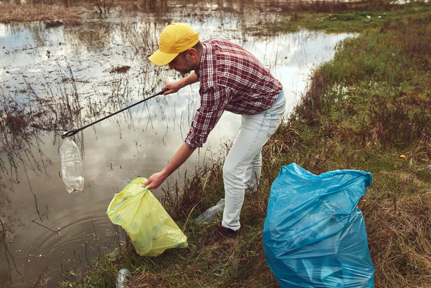 Voluntário e ativista ambiental limpando a costa suja do lago cheio de lixo. - Foto, Imagem