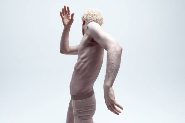 Porträt eines hemdlosen Mannes mit lockigem blondem Haar, der in Unterwäsche posiert und sich isoliert vor weißem Hintergrund von der Kamera abwendet. Konzept der antiken Skulptur, Körperästhetik, Männerschönheit, Kunst - Foto, Bild