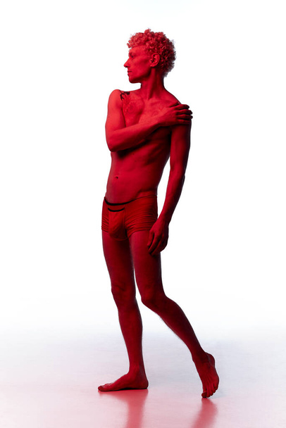 Dromende man met tatoeages op zijn lichaam poserend in standbeeld poseren shirtloos in rode filter geïsoleerd over witte studio als standbeeld. Concept van lichaamsesthetiek, mens schoonheid, creativiteit, inspiratie, kunst, advertentie - Foto, afbeelding
