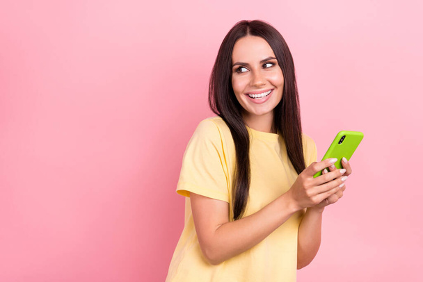 Photo of dreamy sweet lady wear yellow t-shirt texting modern gadget looking empty space isolated pink color background. - Фото, зображення