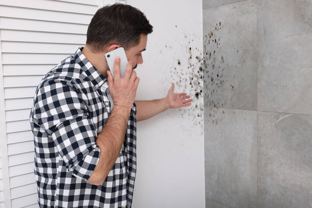 Mold removal service. Man talking on phone and looking at affected walls in room - Fotó, kép