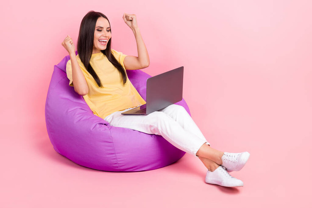 Full length photo of cute lucky lady wear yellow t-shirt sitting bean bag winning game device empty space isolated pink color background. - Photo, Image