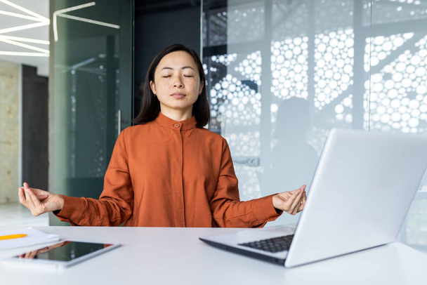 Young beautiful Asian web developer working inside office building, woman resting meditating at workplace with eyes closed, female worker using laptop to write code - Fotoğraf, Görsel