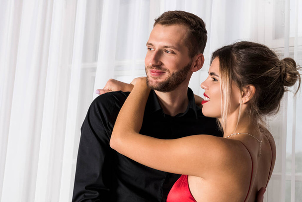 Handsome well dressed young man in black and beautiful woman in red dress are closely looking at each other. The romantic couple exchange loving gazes at each other. - Foto, immagini