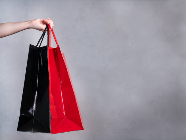 Hand holds red and black shopping bags. Portrait shopping, woman with colored bags - Fotografie, Obrázek