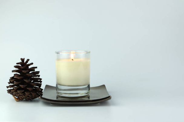 luxury aroma lighting aromatic scented candle glass displayed on golden ceramic holder on white table with pine cone and white cement wall background creat romantic and relax ambient on valentine day - Foto, immagini
