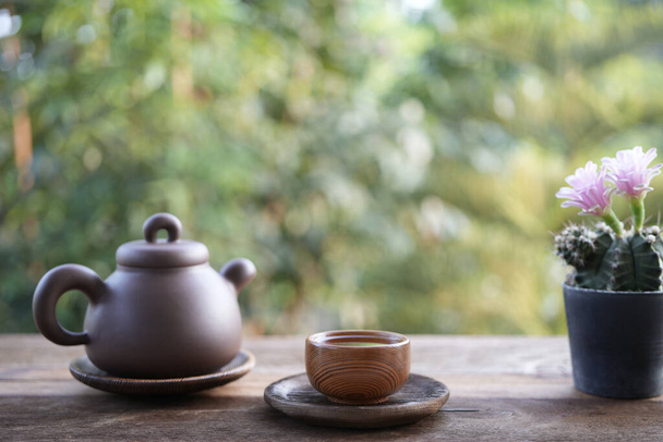 Földi áru teáskanna és teáscsésze és rózsaszín kaktusz virág fa asztalon - Fotó, kép