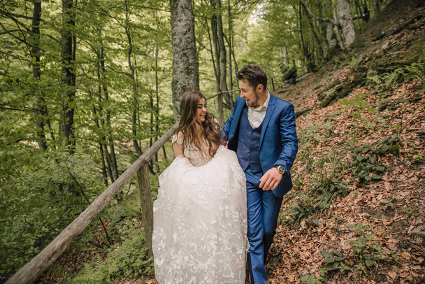 A happy wedding couple is running along a forest path. Groom and bride. Wedding photo session in nature. Photo session in the forest of the bride and groom. - Foto, afbeelding