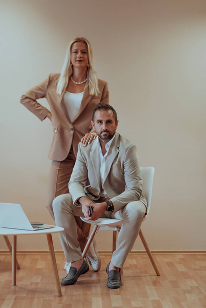 A business couple poses for a photograph together against a beige backdrop, capturing their professional partnership and creating a timeless image of unity and success - Foto, imagen