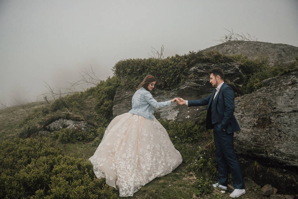 Happy wedding couple in the mountains near a big stone holding hands. Wedding photo session in nature. Photo session in the forest of the bride and groom. - Foto, imagen