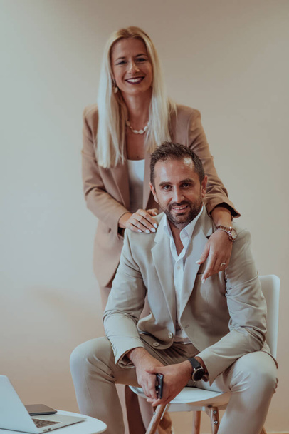 A business couple poses for a photograph together against a beige backdrop, capturing their professional partnership and creating a timeless image of unity and success - 写真・画像