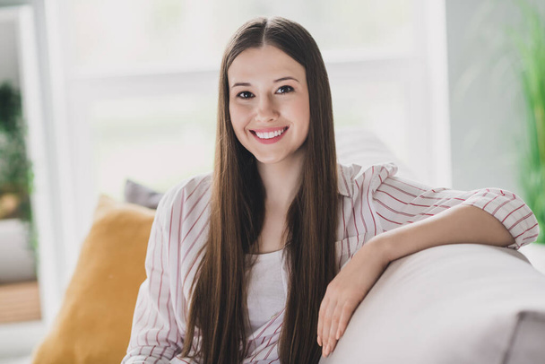 Photo de adorable jeune femme vêtue de rayures chemise assise canapé souriant intérieur maison salle. - Photo, image