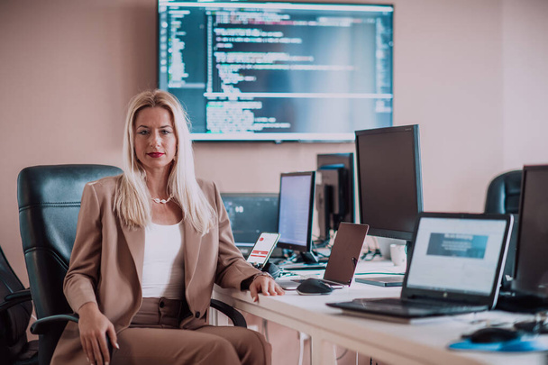 A businesswoman sitting in a programmers office surrounded by computers, showing her expertise and dedication to technology - Фото, зображення