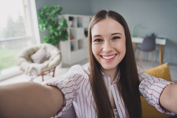 Photo of cheerful charming young lady dressed striped shirt smiling recording apartment tour indoors house room. - Foto, Imagem