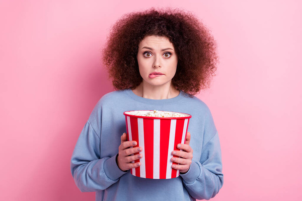 Photo of doubtful scared lady dressed blue pullover biting lip eating pop corn watching scary movie isolated pink color background. - Photo, image