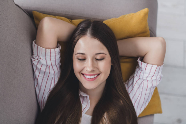 Photo of cheerful sweet young lady dressed striped shirt lying pillow closed eyes arms behind head indoors house room. - Foto, Imagem