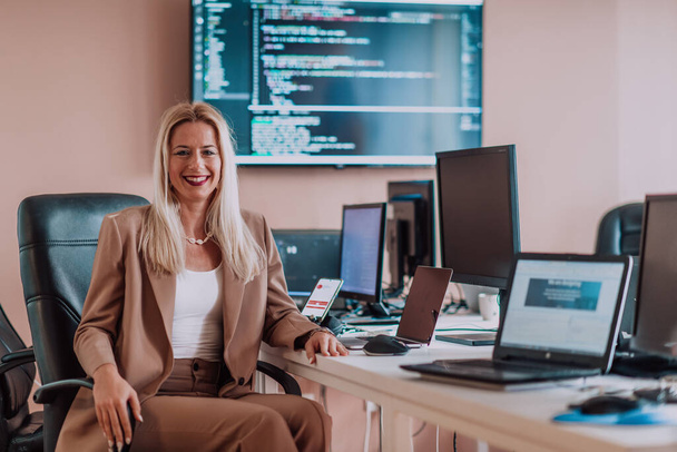 A businesswoman sitting in a programmers office surrounded by computers, showing her expertise and dedication to technology - Fotó, kép