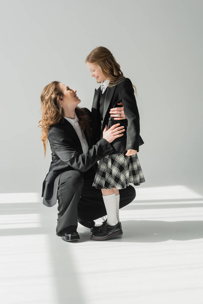 glückliche Mutter und Tochter, Geschäftsfrau im Anzug umarmt Schulmädchen in Uniform mit kariertem Rock, Blazer, bereitet sich auf das neue Schuljahr vor, ermutigt, schaut einander an - Foto, Bild