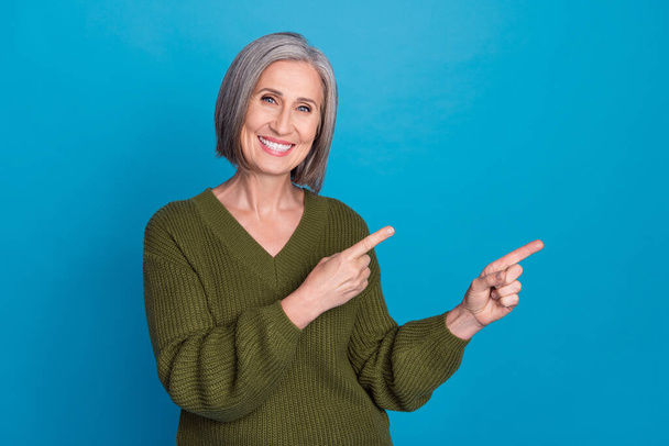 Photo of charming grandmother worker lady direct fingers empty space billboard wear khaki shirt isolated blue color background. - Fotoğraf, Görsel