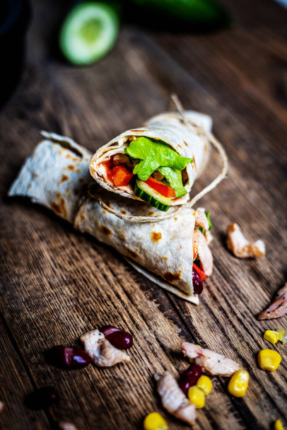 Traditional mexican tortilla wrap with chicken meat and vegetables on wood table - Foto, afbeelding