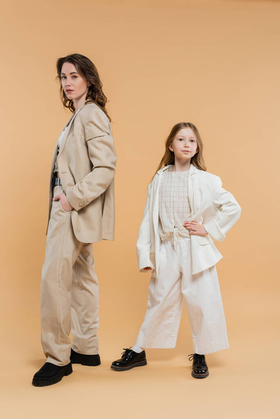 stylish mother child concept, woman in suit and preteen daughter standing in suits on beige background, corporate mom, businesswoman, posing together, hand on hip, business style  - Photo, Image