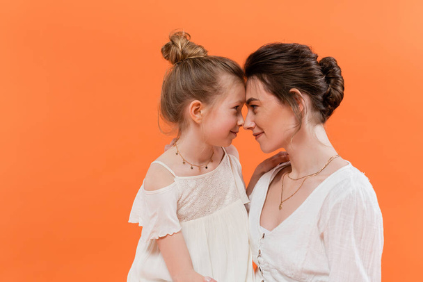 summer trends, mother-daughter bonding, young woman and preteen girl posing on orange background, white sun dresses, togetherness, fashion and style concept, nose to nose - Photo, Image