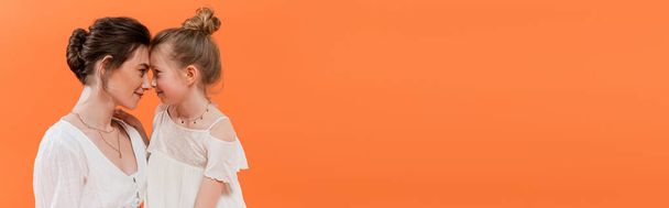 Sommertrends, Mutter-Tochter-Bindung, junge Frau und Frühchen posieren auf orangefarbenem Hintergrund, weiße Sonnenkleider, Zweisamkeit, Mode- und Stilkonzept, Nase an Nase, Banner  - Foto, Bild