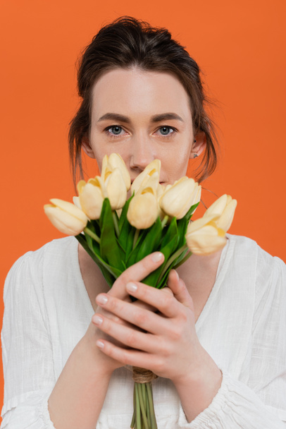 ramo de flores, moda cotidiana, mujer joven en vestido de sol blanco con tulipanes amarillos y de pie sobre fondo naranja, señora en blanco, fondo vibrante, moda, verano  - Foto, imagen