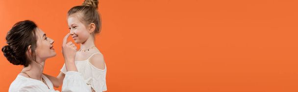 vínculo familiar, mãe feliz tocando nariz da filha pré-adolescente no fundo laranja, vestidos de sol brancos, parentalidade moderna, moda de verão, união, amor, família na moda, banner  - Foto, Imagem