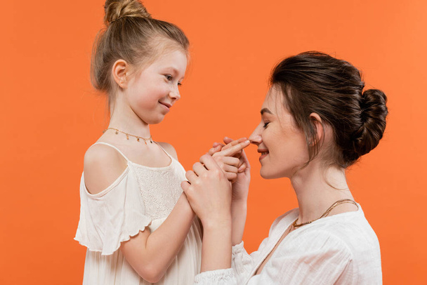 family moment, happy preteen girl touching nose of mother on orange background, white sun dresses, modern parenting, summer fashion, togetherness, love, female bonding  - Foto, imagen