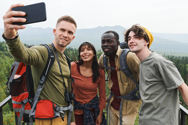 Ομάδα χαμογελαστών νέων πολυεθνικών φίλων πεζοπορίας ποζάρουν για selfie ενάντια στο δασικό τοπίο κατά τη διάρκεια της περιπέτειας - Φωτογραφία, εικόνα