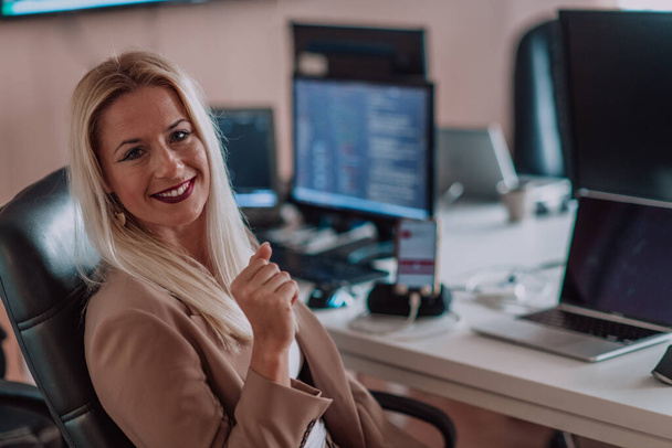 A businesswoman sitting in a programmers office surrounded by computers, showing her expertise and dedication to technology - Fotó, kép