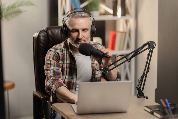 Trabalhador de rádio em camisa quadriculada está usando laptop. Podcast blogger gravação de vídeo com microfone profissional. Foto de alta qualidade - Foto, Imagem