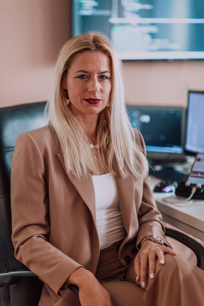 A businesswoman sitting in a programmers office surrounded by computers, showing her expertise and dedication to technology - Zdjęcie, obraz