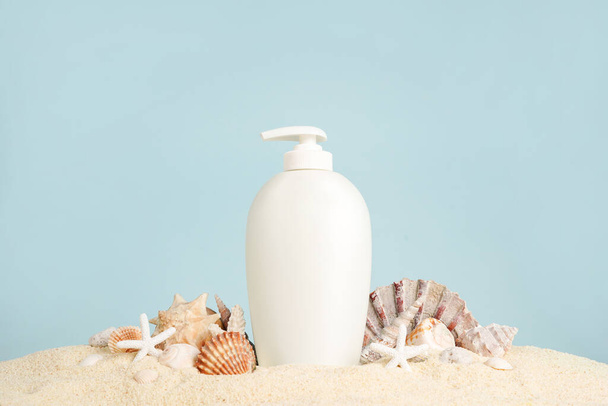 Летний уход за кожей Косметическая бутылка с пулями на песке, синий фон. макет пакета морских натуральных кремов - Фото, изображение
