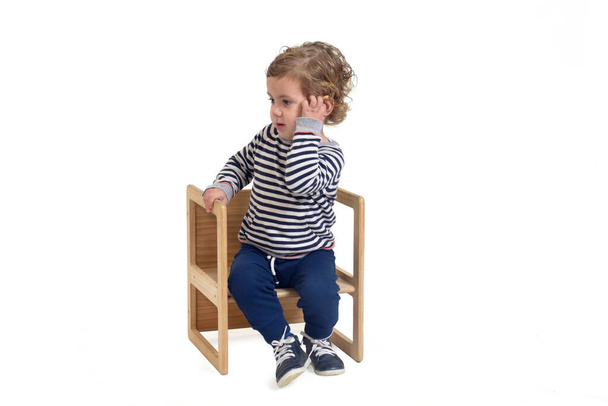 bébé garçon assis sur une chaise avec sa main sur son visage en pensant  - Photo, image