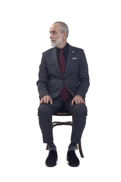 hombre sentado en silla mirando hacia otro lado sobre fondo blanco - Foto, Imagen