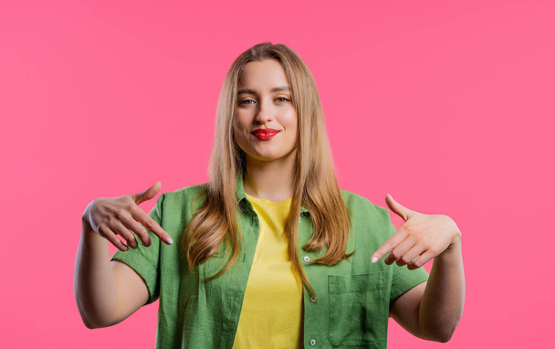 Blonde woman pointing down to advertising area. Pink background. Young blogger asking to click to subscribe below. Copy space for your commercial idea, promotional content. High quality - Foto, immagini