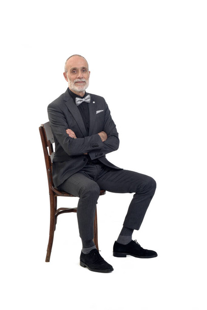 vista lateral de un hombre sentado en silla con traje y pajarita brazos cruzados sobre fondo blanco - Foto, Imagen