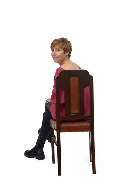 zpět pohled na ženu v těsné džínové kalhoty sedí na židli kříž nohy a otočil a při pohledu na kameru na bílém pozadí - Fotografie, Obrázek
