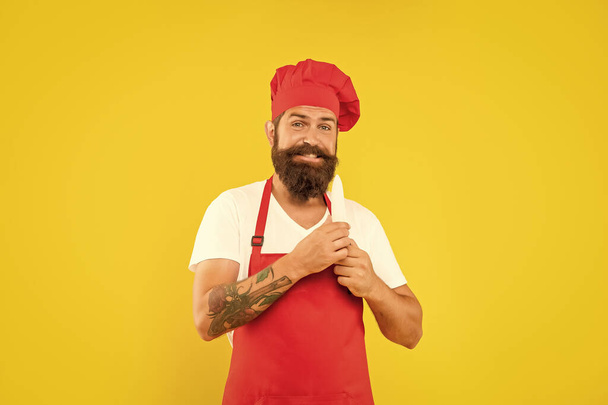 Happy man in red apron and toque holding chefs knife yellow background, chef. - Foto, afbeelding