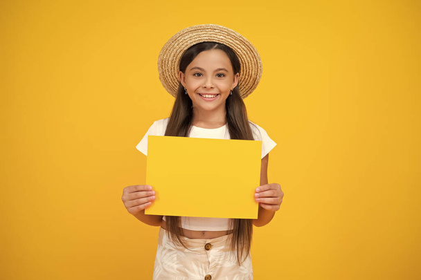 happy teen girl hold empty advertisement paper with copy space on yellow background. - Foto, afbeelding