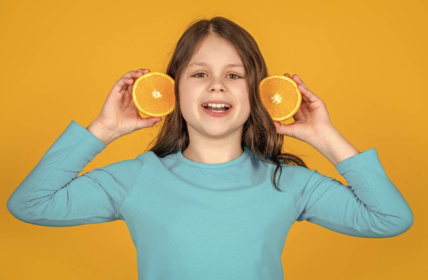 glad teen girl hold orange fruit on yellow background. - 写真・画像