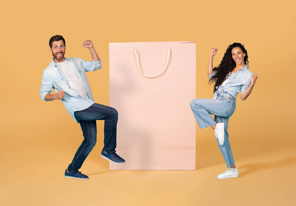 Happy emotional young woman and man wearing casual outfits gesturing next to huge shopping bag, celebrating season sale or black friday, colorful background, mockup, copy space, collage - Photo, image